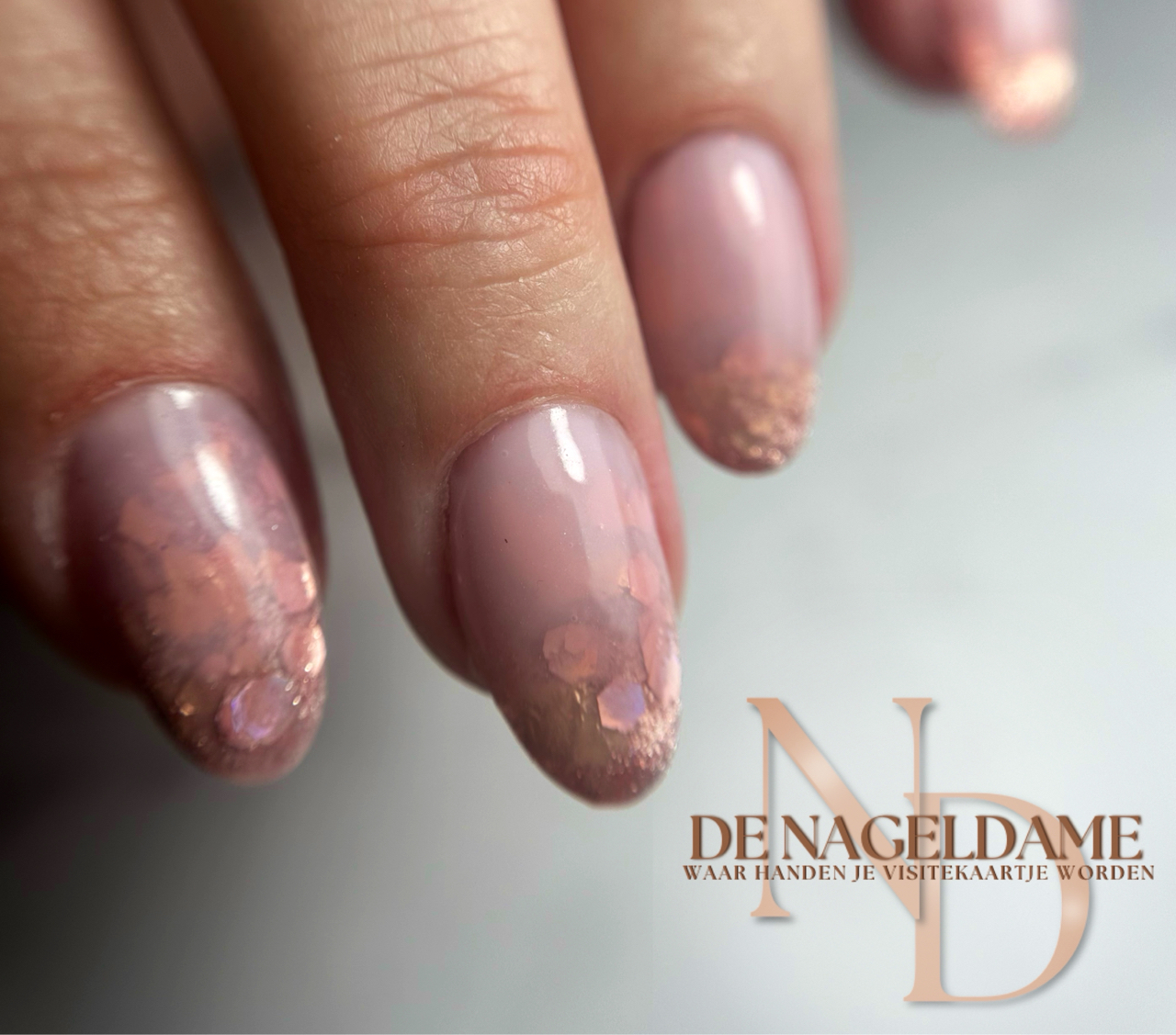 Nude nagels met roségouden glitter, met het logo van De Nageldame